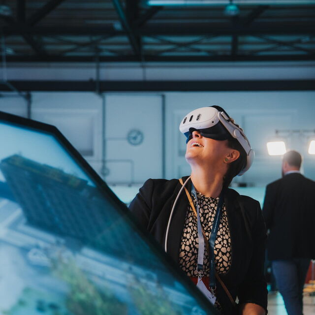 Susanne Stump von futureSAX betrachtet auf der sächsischen Innovationskonferenz durch die VR-Brille das Innere einer bepflanzten Schwimminsel und staunt.