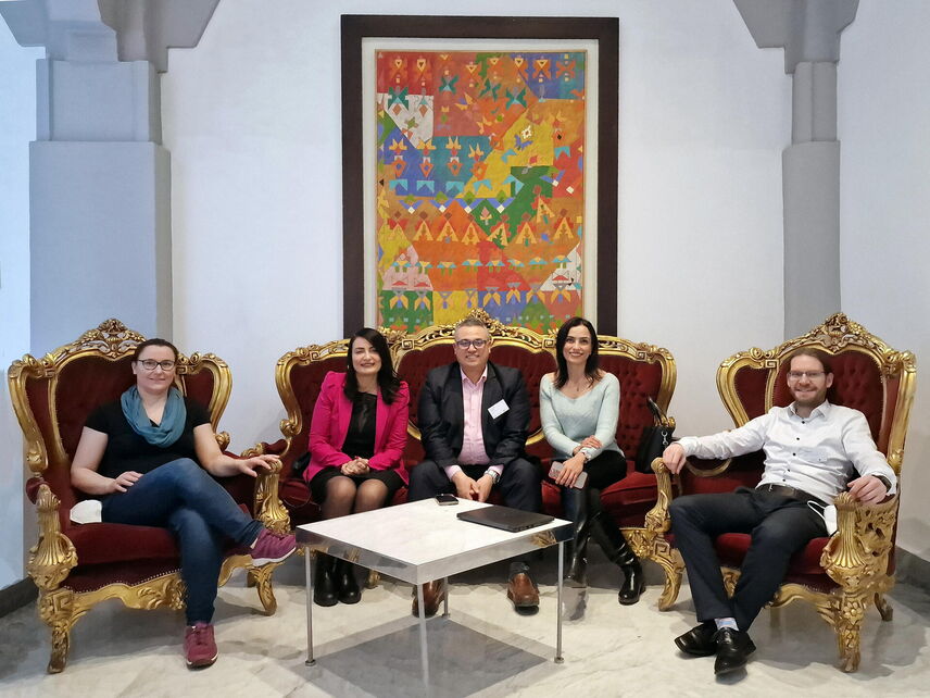 5 Personen sitzen auf Sesseln vor einem Bild