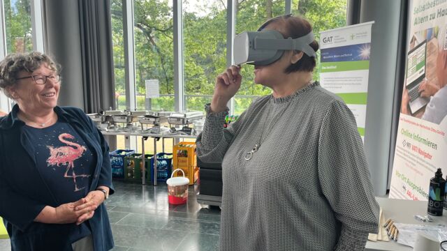 Zwei Seniorinnen, eine von ihnen probiert eine VR-Brille aus