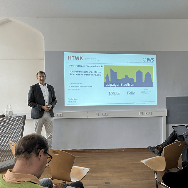 Referent Tilo Saßbach steht vor einer Präsentationsfolie mit dem Titel „Leipziger BlauGrün“ im Veranstaltungsraum der Hochschule Zittau/Görlitz; im Vordergrund sitzen Teilnehmende des Fachaustauschs.