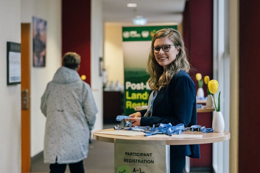 Eine Frau, die an einem Stehtisch steht. Im Hintergrund eine Person.