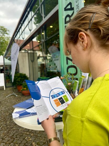 Eine Frau, die an einem Stehtisch steht und einen Flyer anschaut.