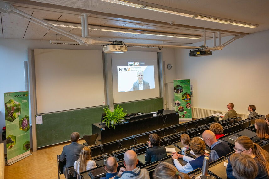 Ein Mann, der Digital dazugesschalten ist, und ein Grußwort zu der Veranstaltung hält.