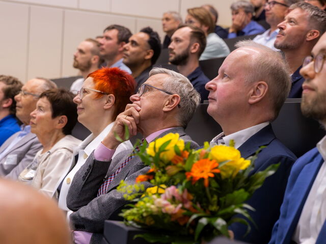 Menschen sitzen im Hörsaal und schauen in Richtung Bühne