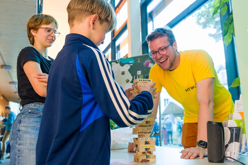 Ein Mann und ein Junge spielen das Spiel Jenga. Eine Frau schaut zu.