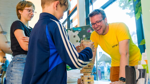 Ein Mann und ein Junge spielen das Spiel Jenga. Eine Frau schaut zu.
