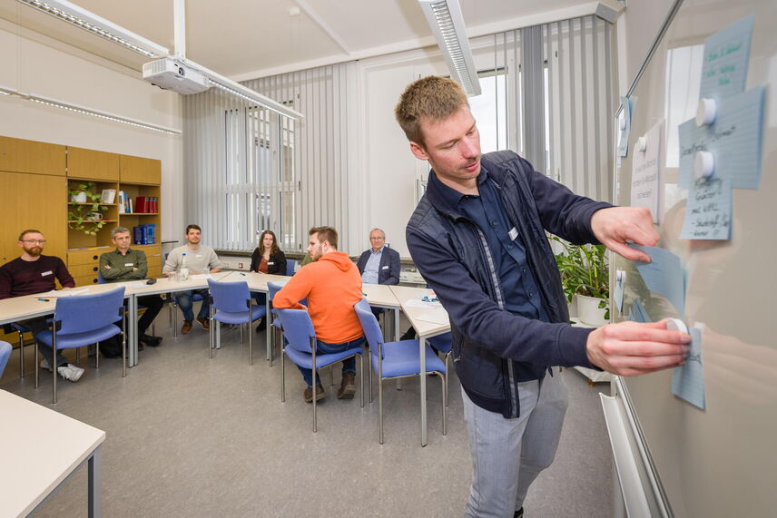 Lucas Kurzweg hängt Karteikarten an ein Whiteboard. Teilnehmende sitzen im Hintergrund.
