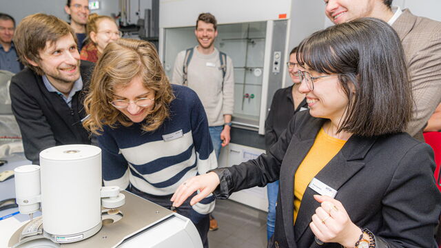 Eine Mitarbeiterin der HTWD zeigt den Besucher*innen eine Apparatur im Labor.