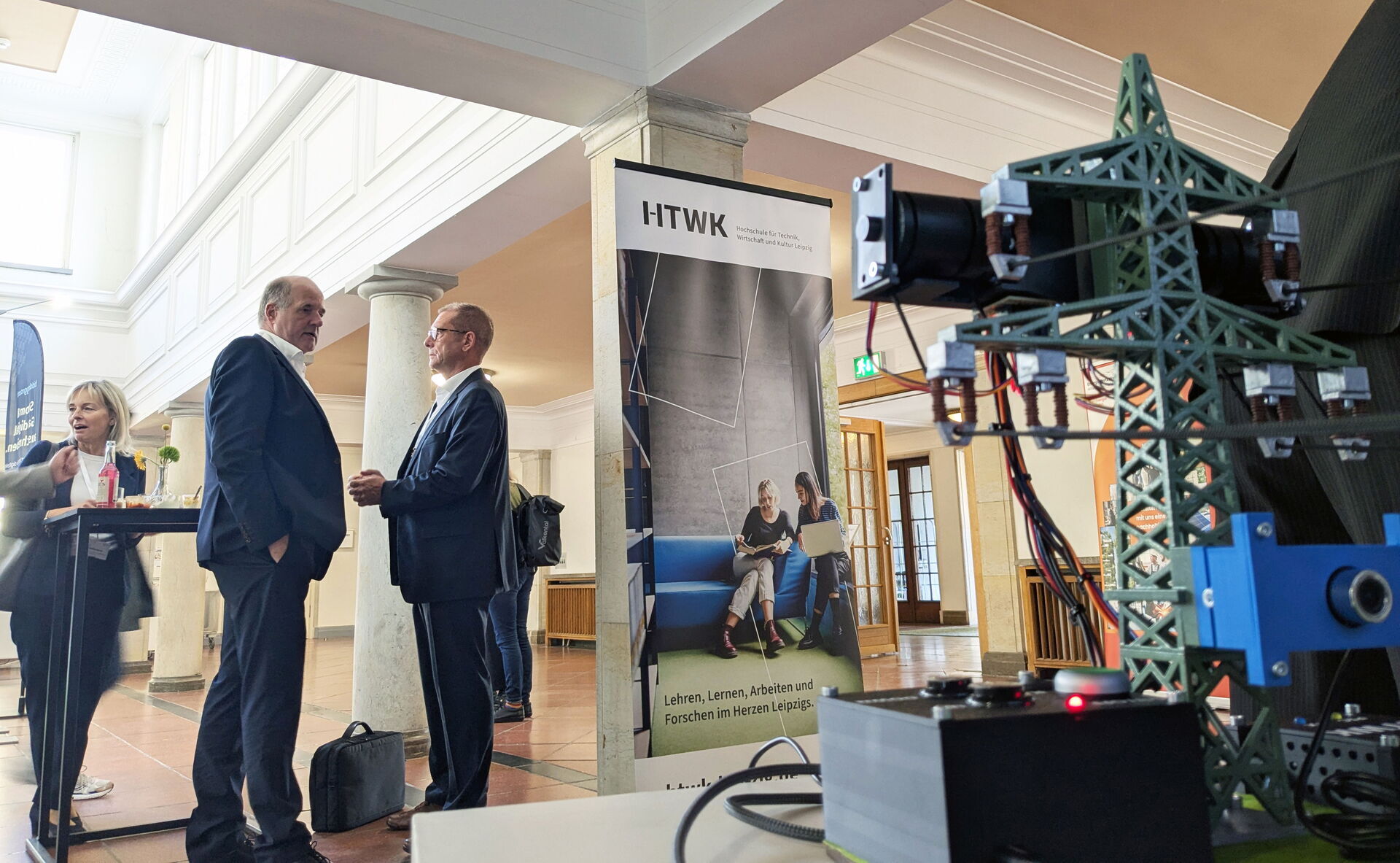 Modell mit Stromtrasse im Vordergrund, im Hintergrund Ausstellende und Besuchende