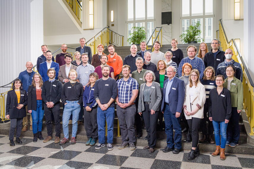 Teilnehmende und Persönlichkeiten der HTW als Gruppe vor einer Treppe.