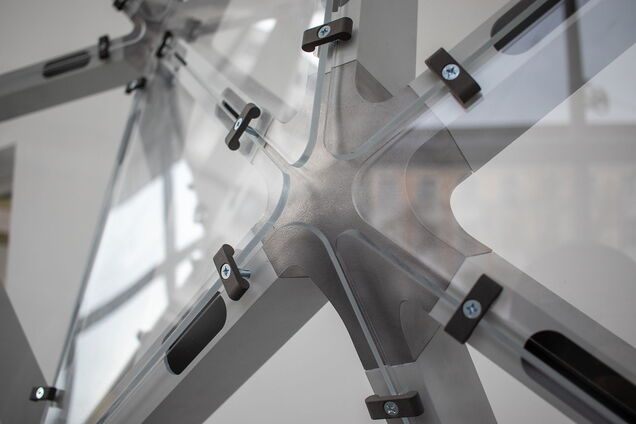 Knotenpunkt aus Metall von dem sechs Streben wegführen, die dabei enstehenden Flächen sind mit einem druchsichtigen, glänzenden MAterial überspannt