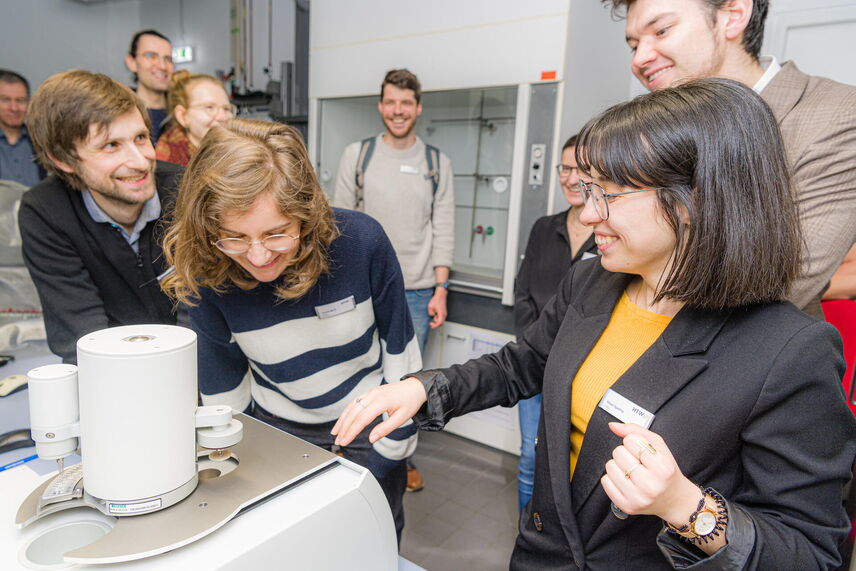 Eine Mitarbeiterin der HTWD zeigt den Besucher*innen eine Apparatur im Labor.