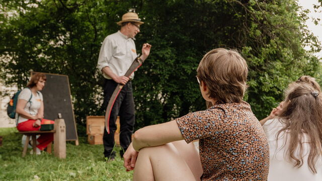 Frauen, die zu einem Mann schauen, der ein Sensenblatt in der Hand hält.