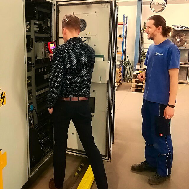 Zwei Männer stehen vor einem Gerätekasten, dessen Wärme kontrolliert wird.