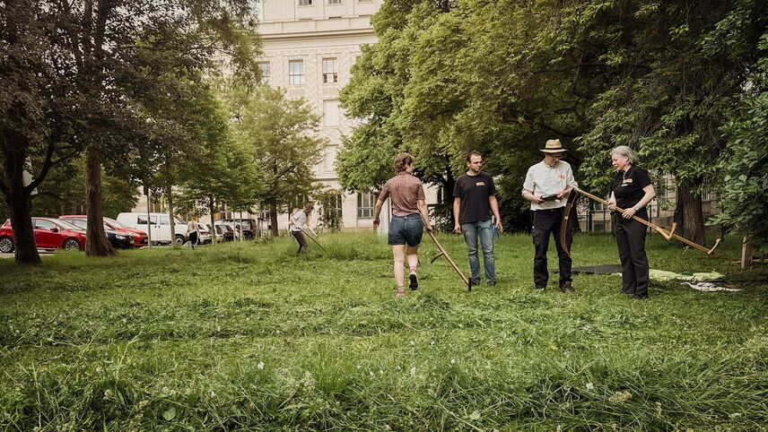 Menschen mit Sensen auf einer Wiese, die sich unterhalten