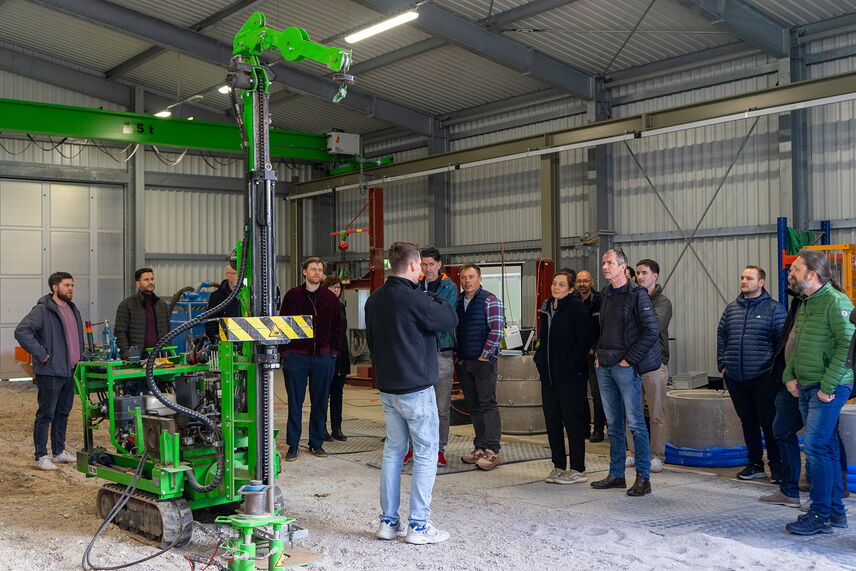Ein Mann steht einer Gruppe von Menschen gegenüber, daneben ein großes grünes Gerät, im Geotechnikum der HTWK