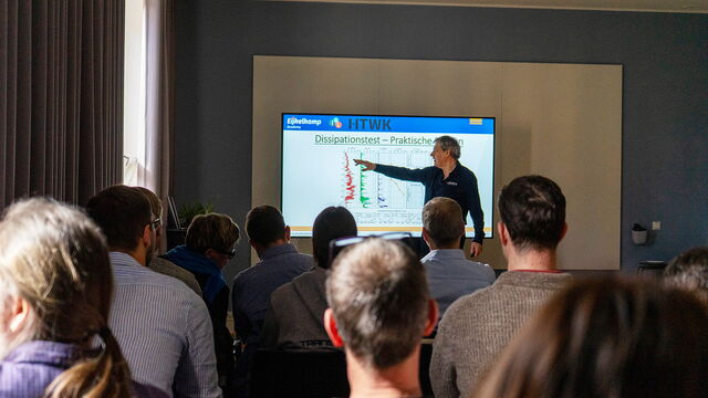 Ein Mann steht vorne im Seminarraum und erklärt Inhalte vor Publikum am Bildschirm