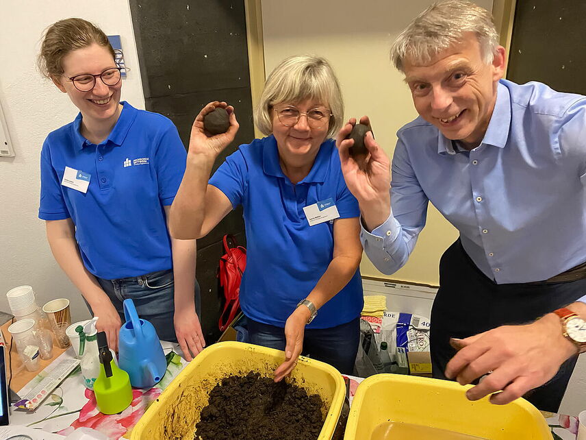 Drei Personen stehen am Tisch und formen kleine Saatbomben.