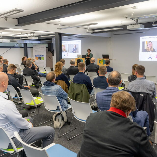 Sophie Tietze eröffnet Jahrestreffen mit einer Präsentation und im Publikum sitzen die Teilnehmenden