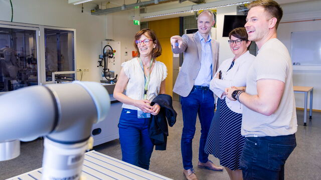 4 Personen lachen und bestaunen einen Roboter.