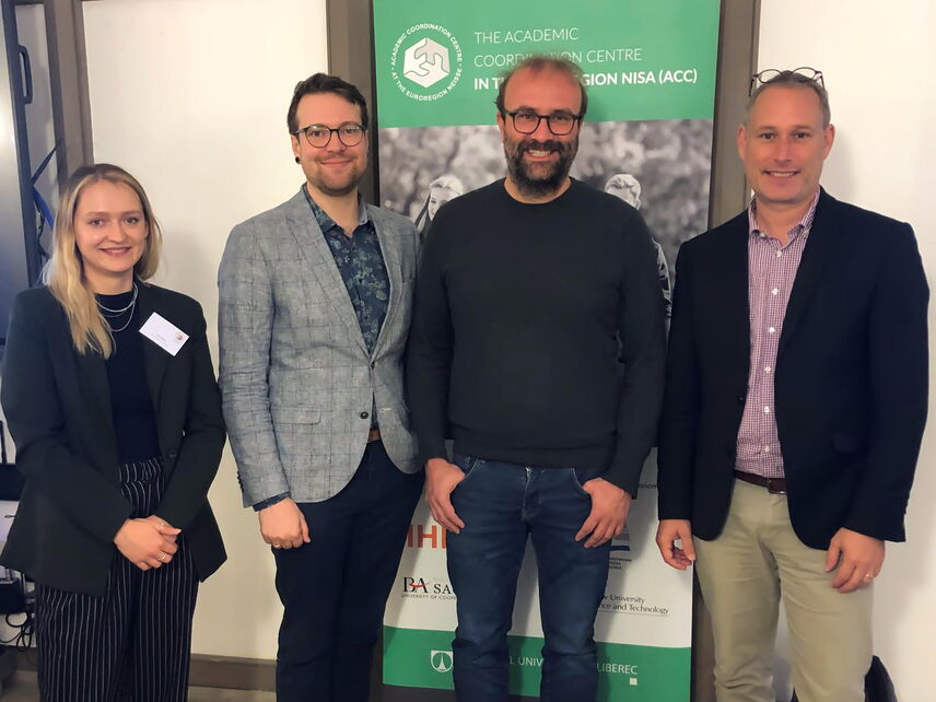 Vier Menschen die vor einer grün-weißen Fläche stehen.