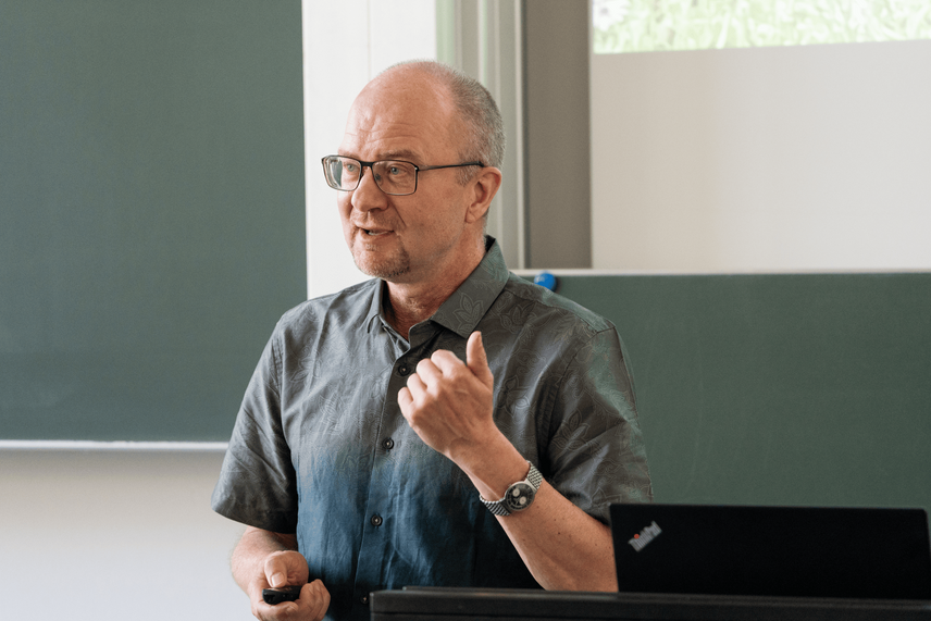 Ein sprechender Man in einem grünen Hemd, vor einer grünen Tafel