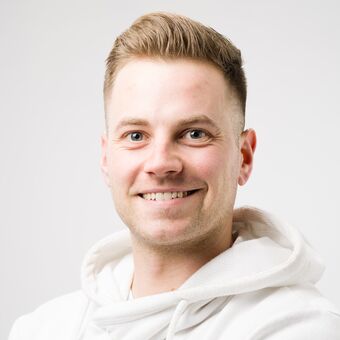 Ein Portraitfoto von Tom Richard Pilk in einem weißen Hoodie vor einem weiß-grauen Hintergrund