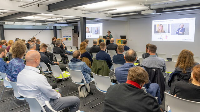Sophie Tietze eröffnet Jahrestreffen mit einer Präsentation und im Publikum sitzen die Teilnehmenden