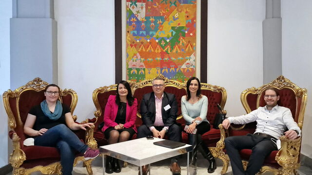 5 Personen sitzen auf Sesseln vor einem Bild