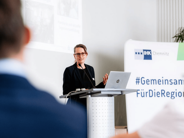 Professorin Julia Zähr steht am Pult und spricht zum Publikum.