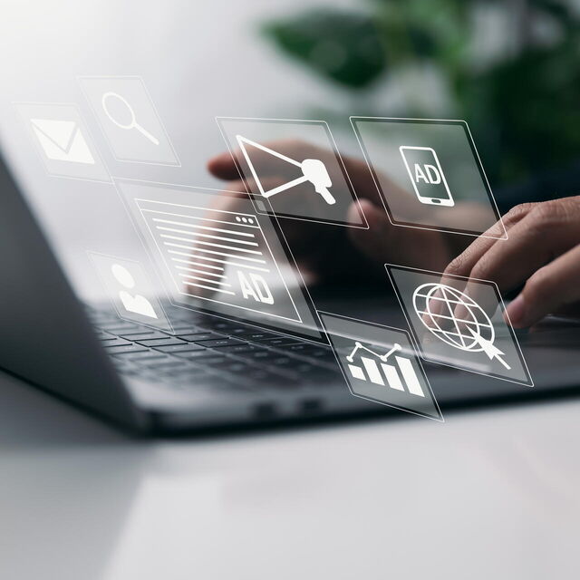 Fotomontage von auf einem Laptop tippenden Fingern, über der Tastatur sind durchscheinende Icons zu sehen