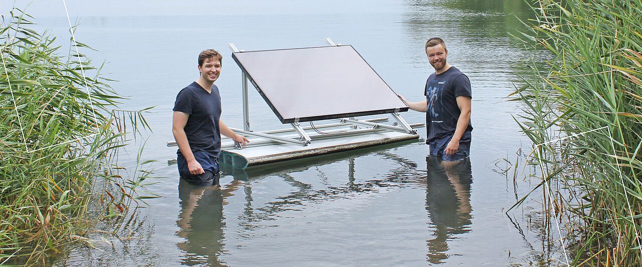 Zwei Männer stehen im See und in der Mitte schwimmt ein Solarmodul