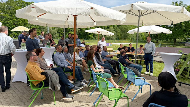 Blick auf die Teilnehmenden, die auf der Terrasse des ubineums unter Sonnenschirmen sitzen und den Pitches folgen.