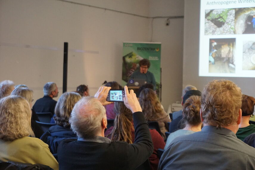 Ein Mann, der während eines Vortrags ein Foto mit dem Smartphone macht.