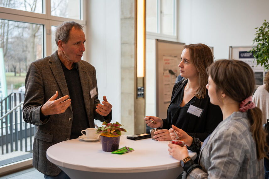 Drei Menschen die an einem Tisch stehen und sich unterhalten