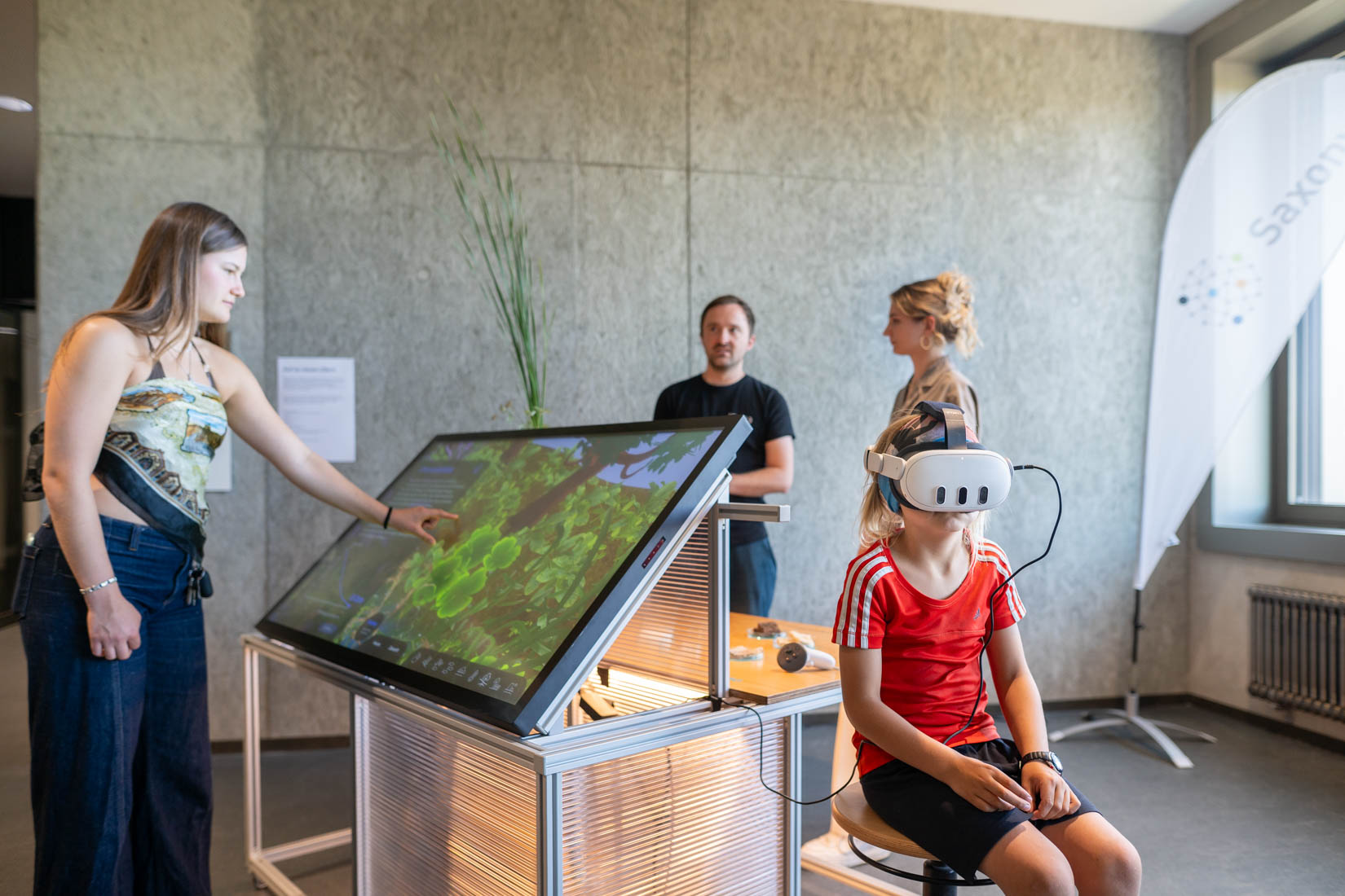 Bei "Auf zu neuen Ufern" kann das Exponat von drei Seiten gleichzeitig entdeckt werden. Mehrere Leute stehen um das Exponat. Eine Person tippt auf dem Bildschirm, ein Kind trägt die VR-Brille.