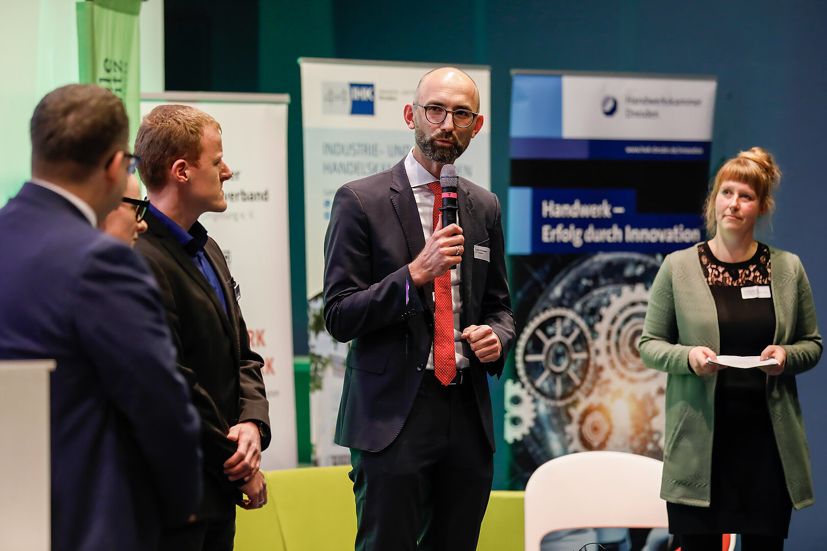 Fünf Personen stehen auf der Bühne, ein Mann spricht ins Mikrophon