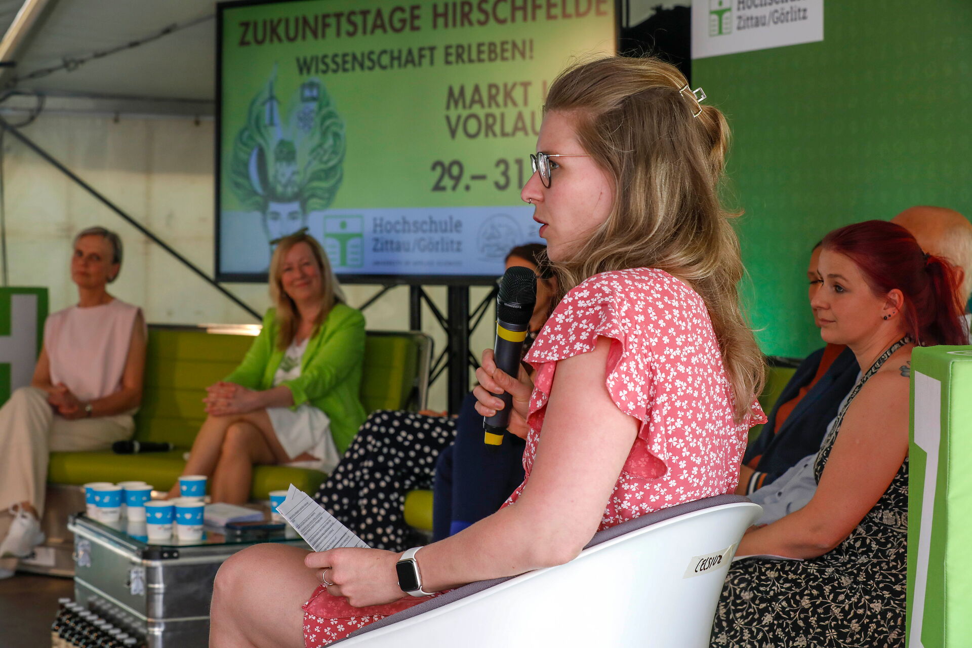Franziska Stölzel moderiert mit Mikrofon eine Podiumsdiskussion.