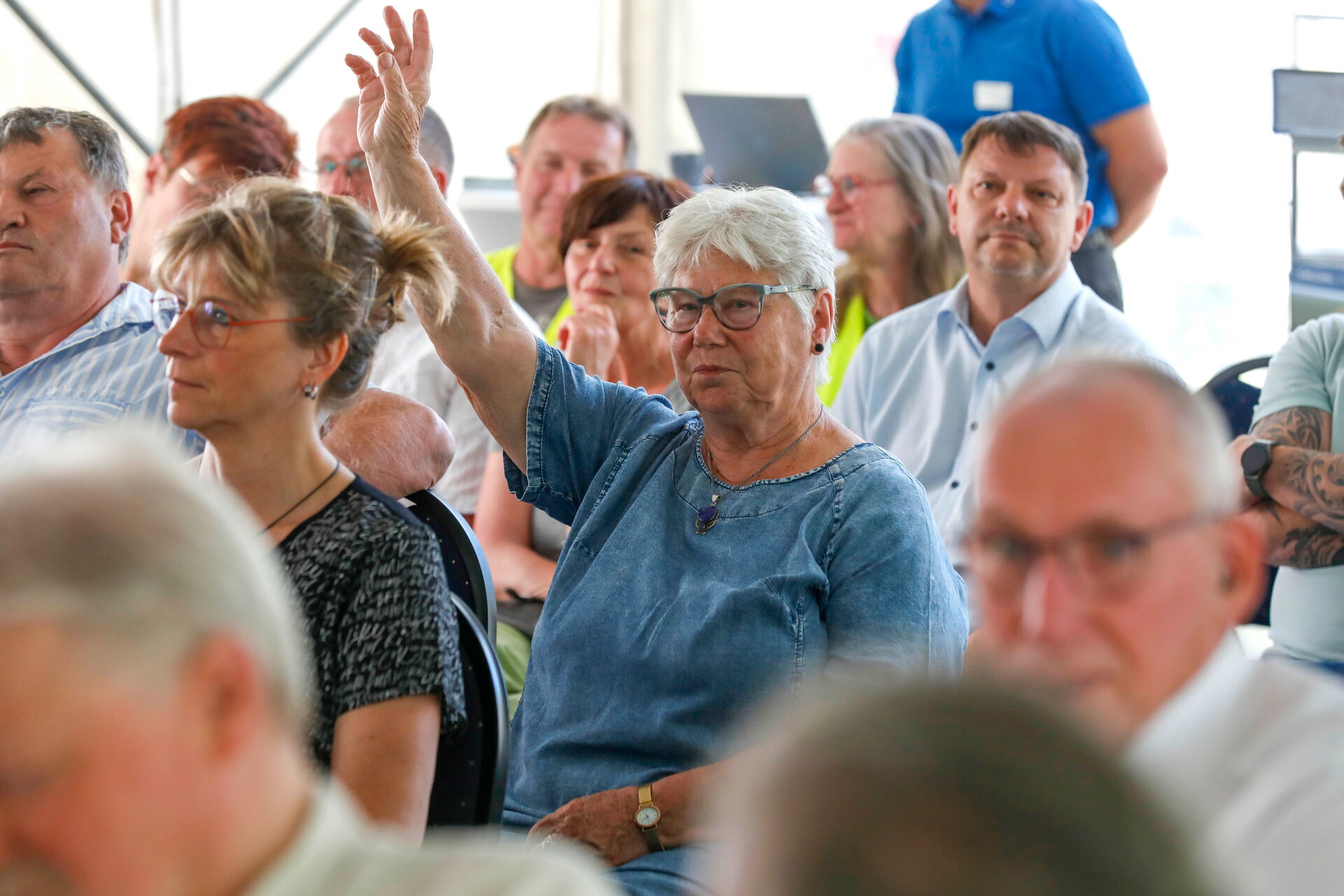 Eine Frau hebt während einer Veranstaltung im Publikum die Hand.