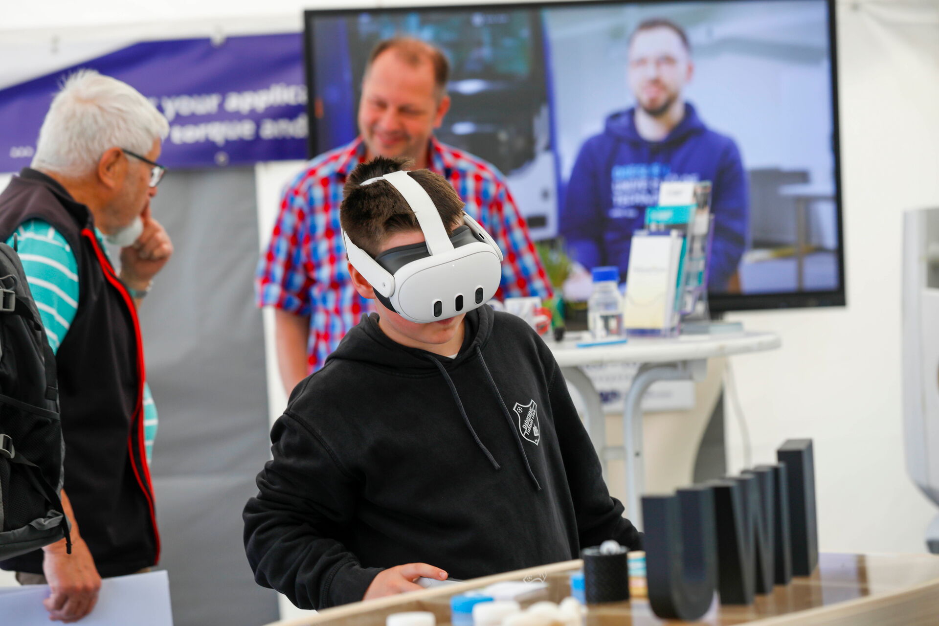 Ein Junge mit VR-Brille steht vor einem Tisch mit verschiedenen schwarzen Spielelementen.
