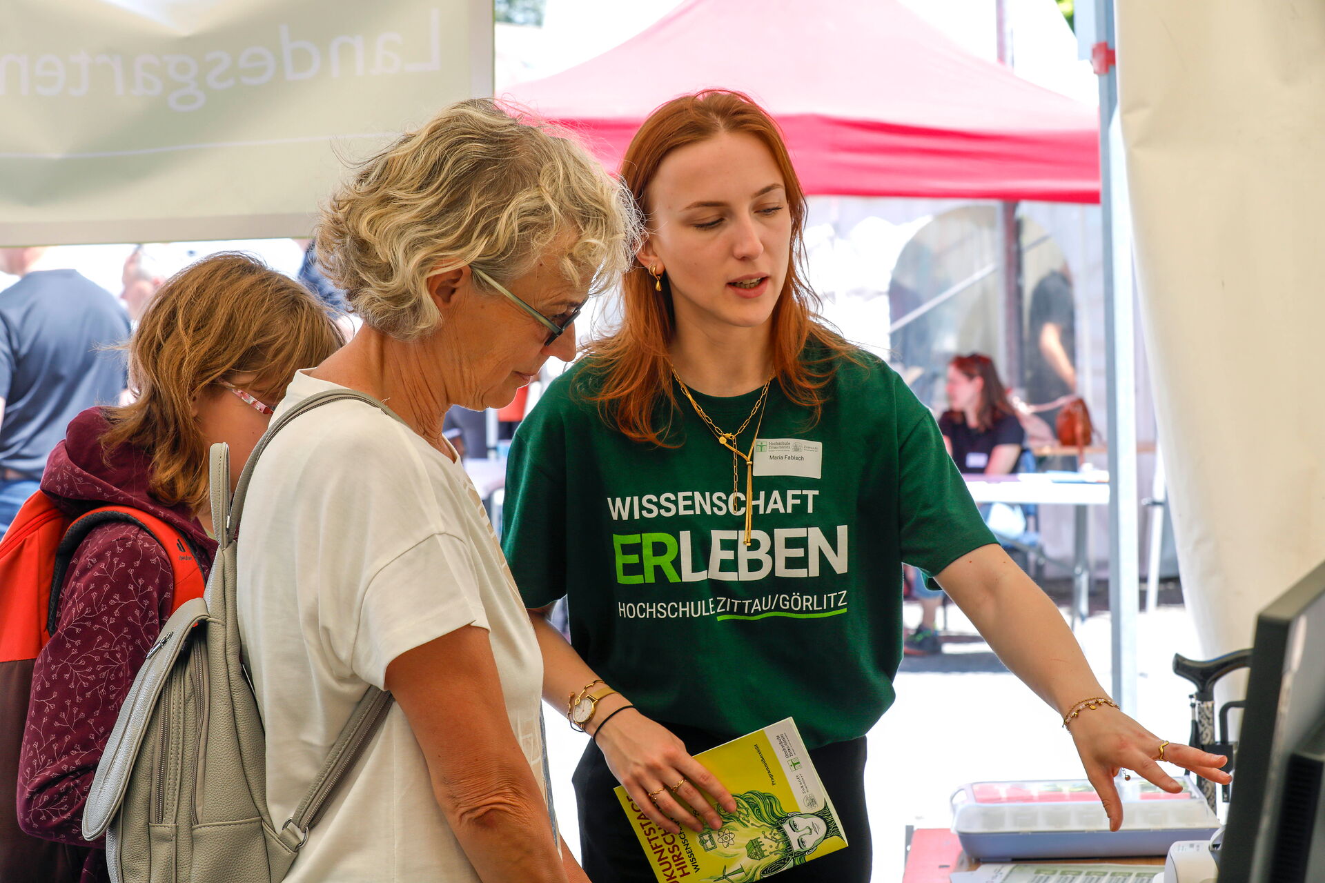 Eine junge Frau erklärt zwei Besucherinnen ein Exponat an einem Informationsstand.