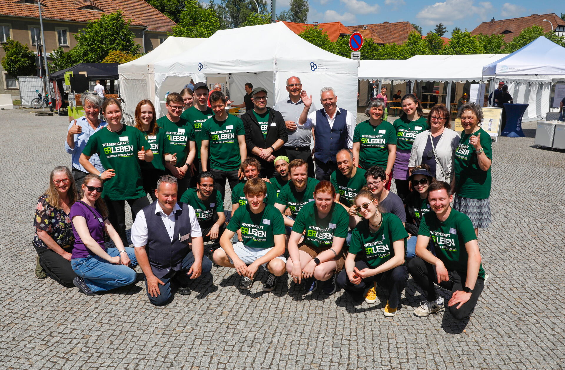 Eine große Gruppe von Mitwirkenden posiert gemeinsam auf dem Hirschfelder Marktplatz.