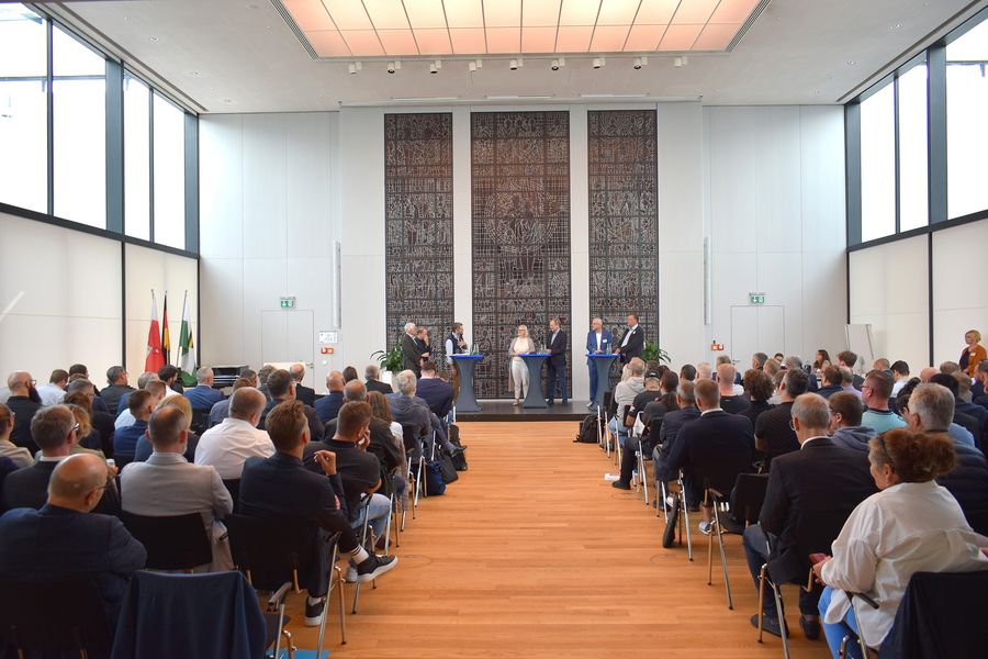 Blick von hinten durch den Bürgersaal auf die Teilnehmenden und das Podium.
