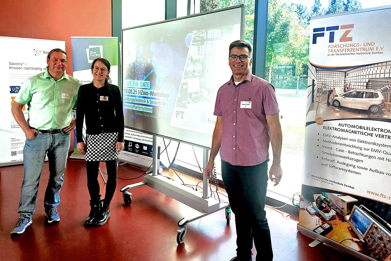 Beim Workshop im „Forum Mobile“ der WHZ wurde unter anderem neue Wasserstoffmesstechnik präsentiert. V. l. n. r.: Dr. Gert Schlegel (HZwo e V.), Ulrike Riemer (WHZ/Saxony⁵), Matthias Trebeck (WHZ/Saxony⁵) (Foto: Ivonne Mallasch/FTZ e. V.) Drei Personen umrahmen ein großes Display. Im Hintergrund und auf der rechten Bildseite befinden sich Rollups.