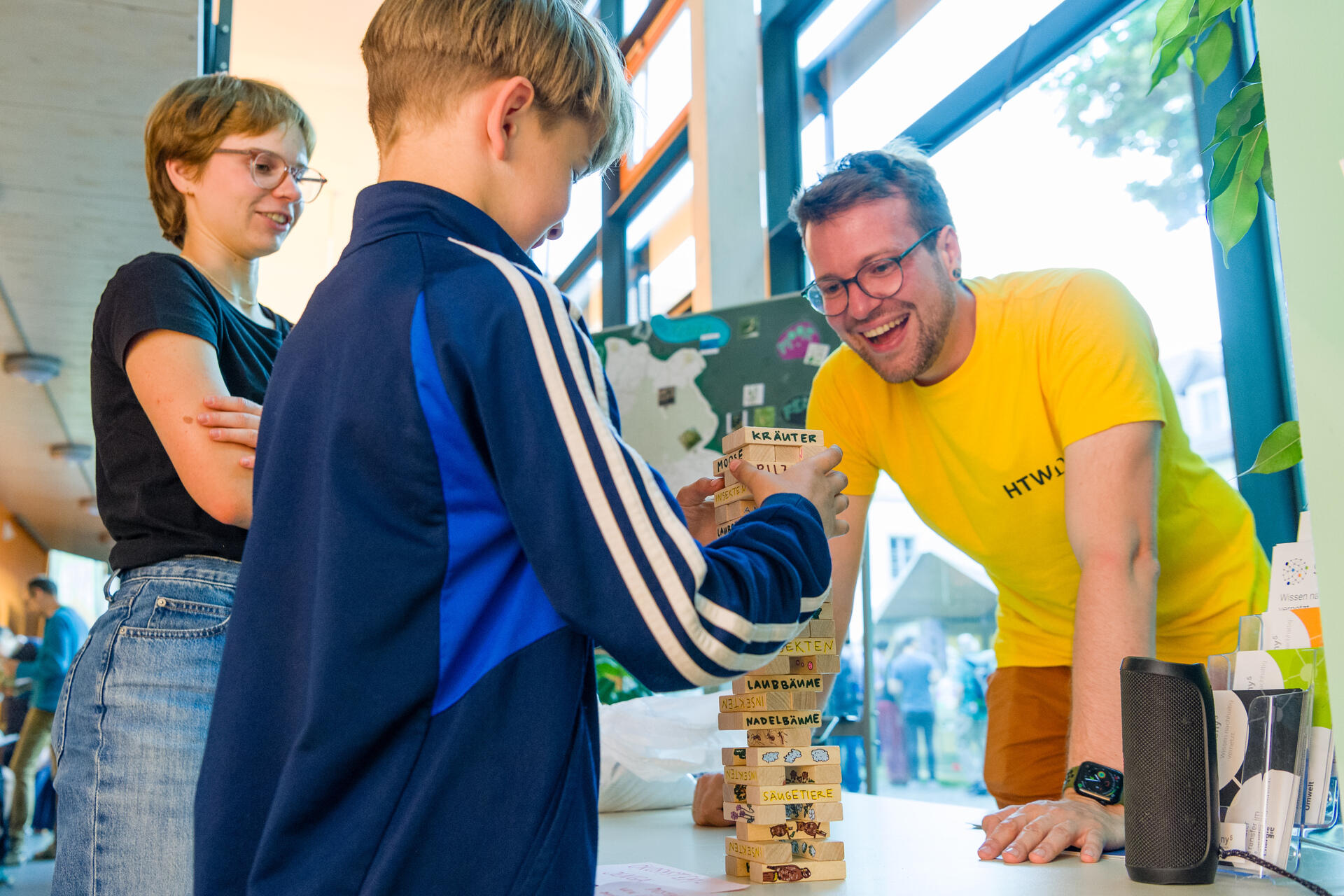 Nico Beier vom BIOZENTRA und ein Junge spielen das Spiel Jenga. Eine Frau schaut zu.