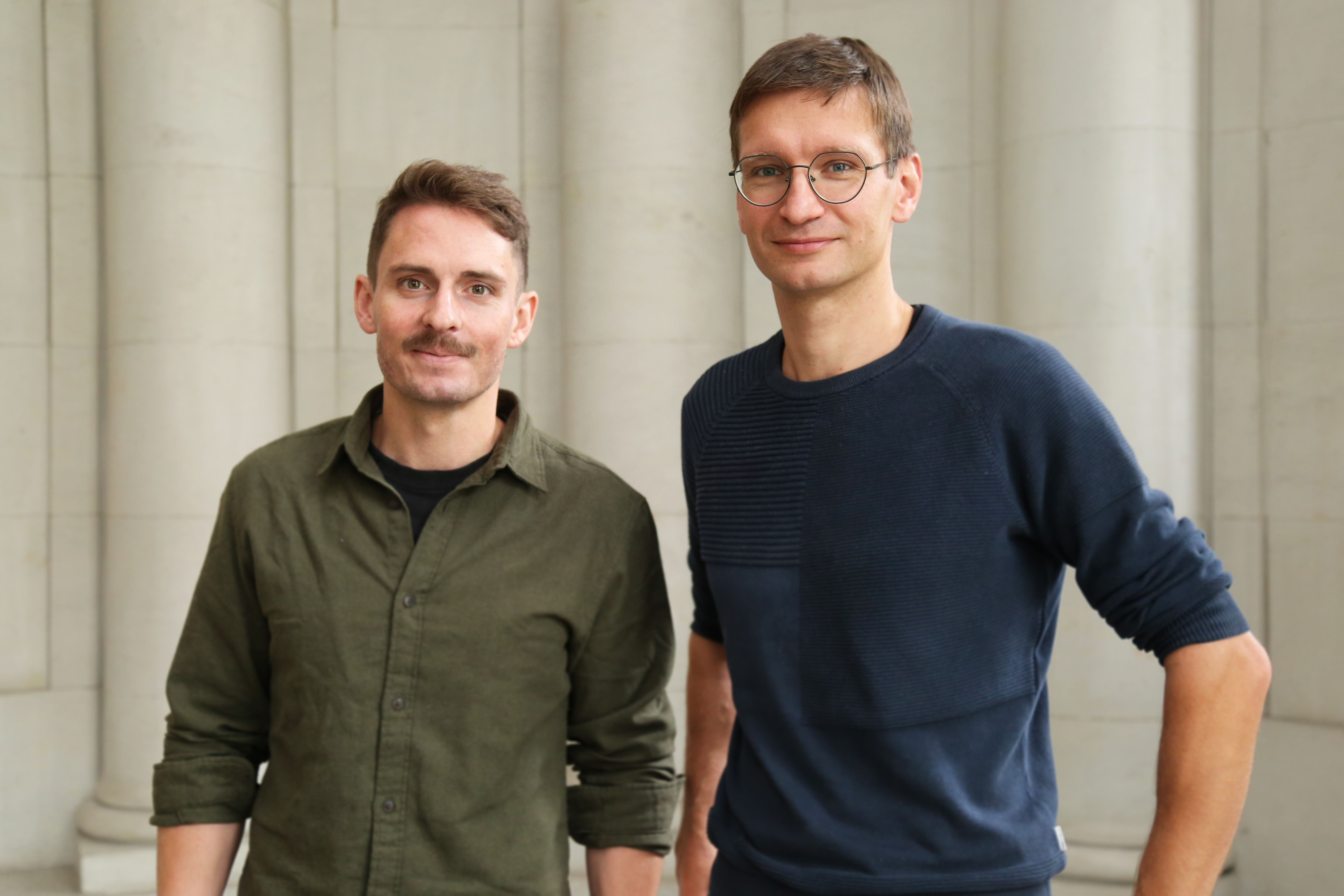 Bénédict Löwe und Dr.-Ing. Alexander Knut stehen vor einem Hintergrund mit weißen Säulen.